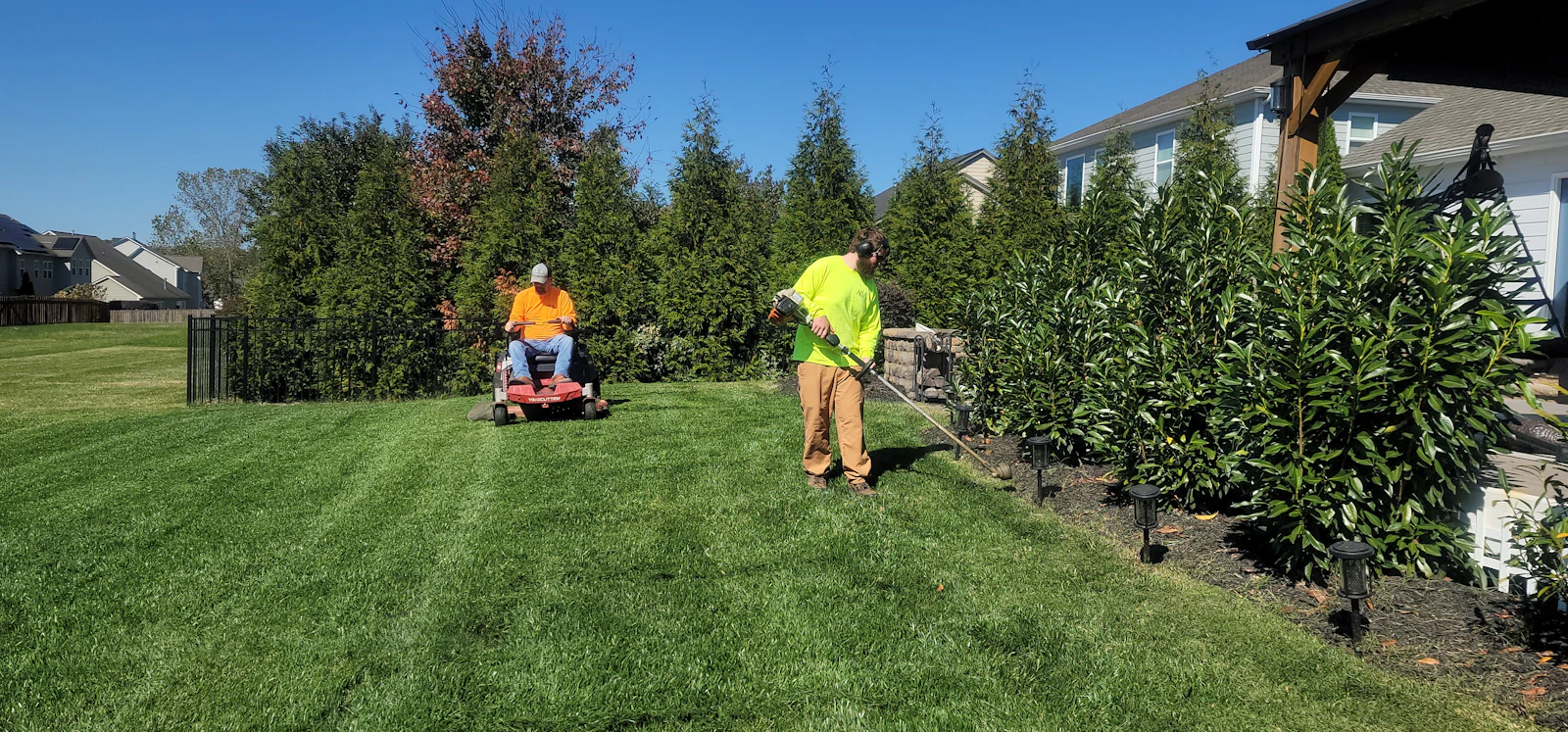 Two landscapers mowing and trimming a residential lawn. Unsplash sample photo.